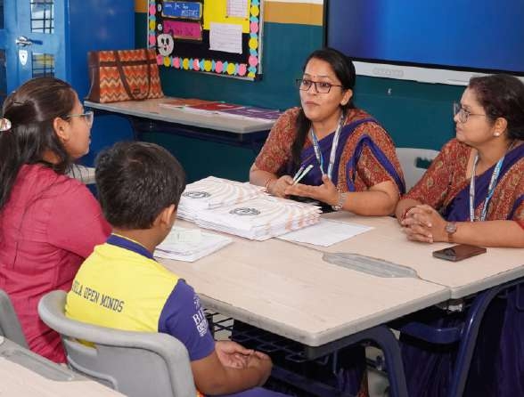 Teachers discussing development with parent in red and young learner