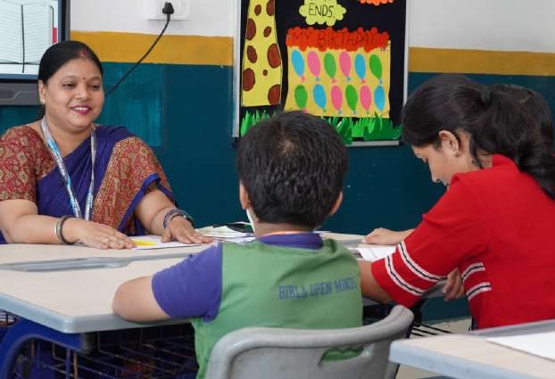 Teacher smiling across the desk with mother in red and child in green