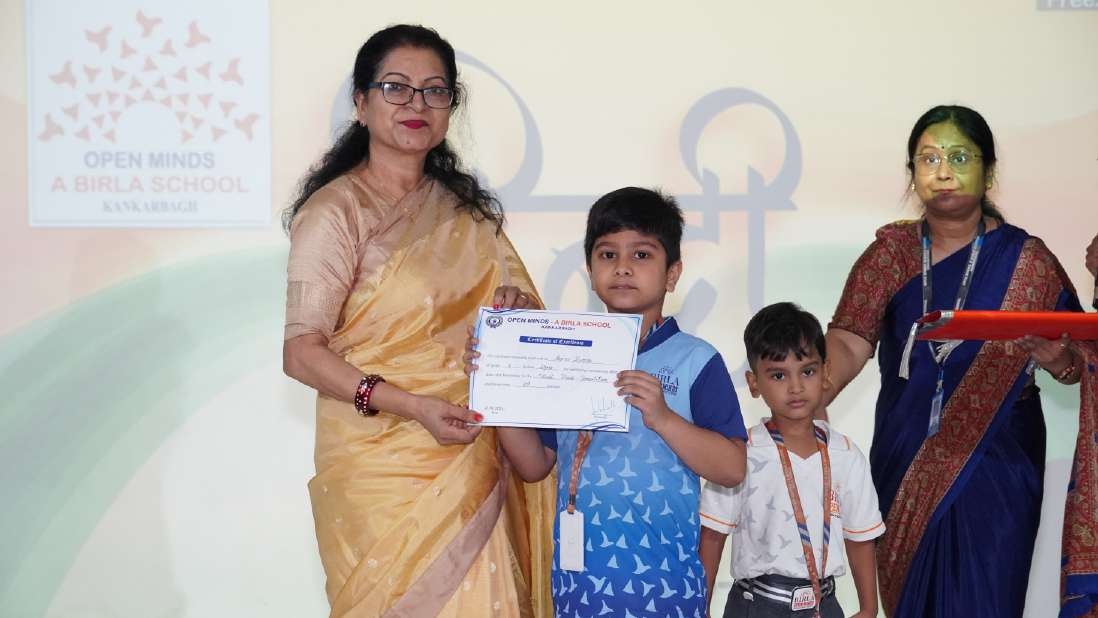 Teacher in yellow saree presenting certificate of merit to boy