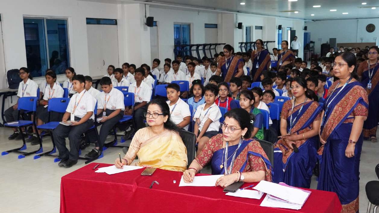 Judges at red tablecloth table evaluating while auditorium students watch intently