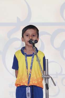 Primary boy in yellow and blue sportswear reciting at microphone